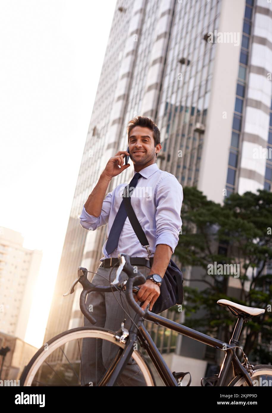 Ill be there in 10. a businessman taking a phone call while commuting to work with his bicycle. Stock Photo