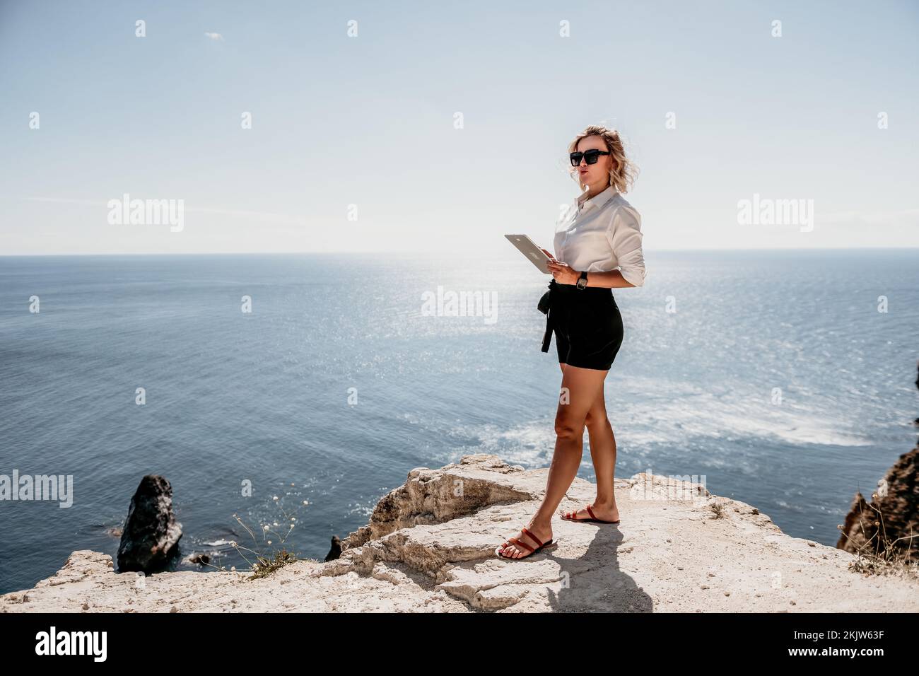 Digital nomad, Business woman working on tablet pc pad computer by the sea. Pretty lady with tablet pc on the sea, makes a business transaction online Stock Photo