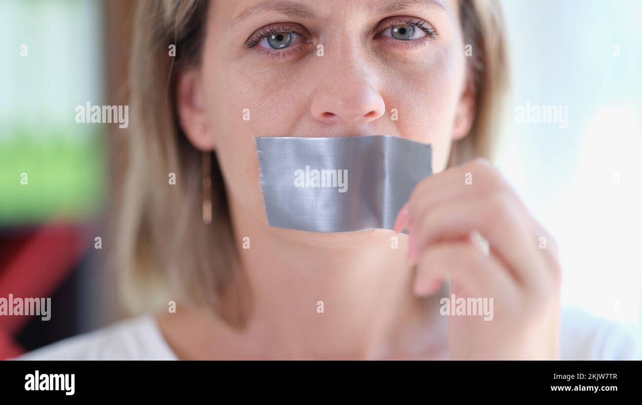 Young woman unsticking duct tape on mouth Stock Photo