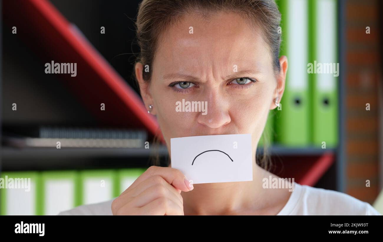 Grumpy woman covering face with paper unhappy emoticon symbol Stock Photo