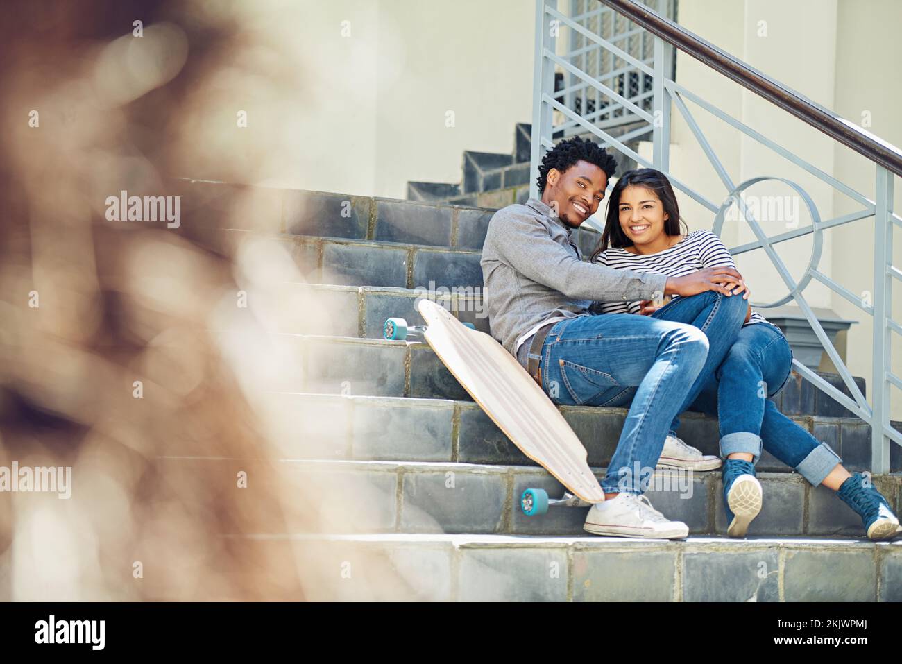 Couple, happy and skateboard while sitting on stairs with hug, love and romance in city sunshine. Black couple, urban happiness and outdoor with Stock Photo