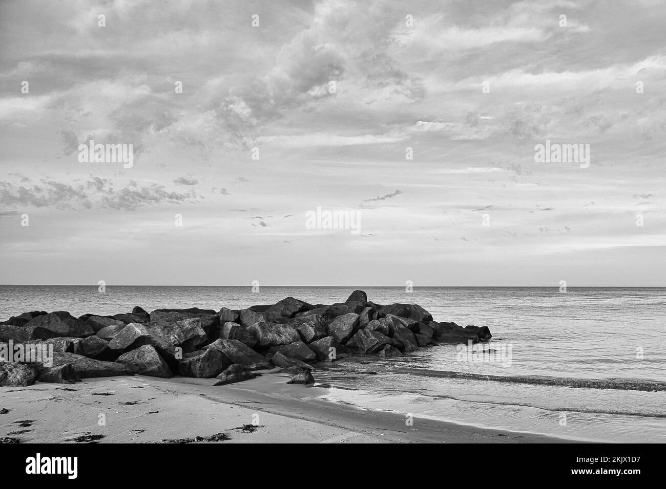 Stone groyne jutting into the sea in Denmark with clouds in the sky taken in black and white. Coastal landscape in Denmark. Landscape photo from ocean Stock Photo