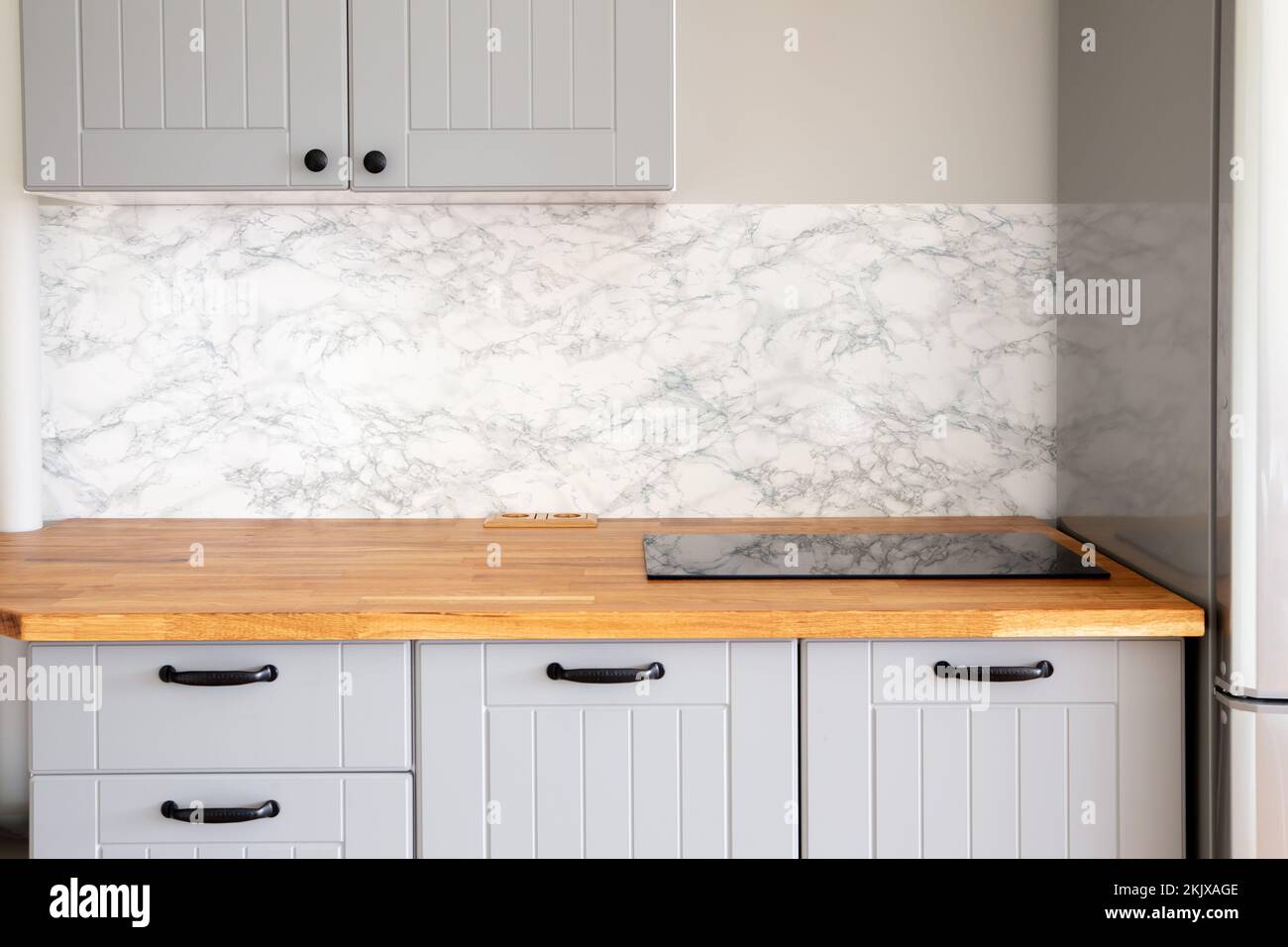 Empty modern minimal grey color kitchen, marble wall, solid natural wood butcher block countertop with built in small stove, black handles. Stock Photo