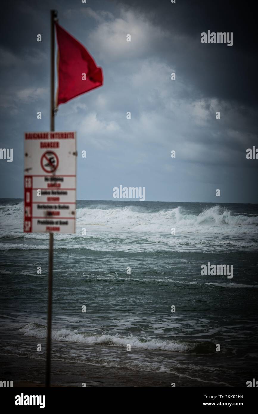 Danger Red Flags fly on the beach as rough seas break waves up the
