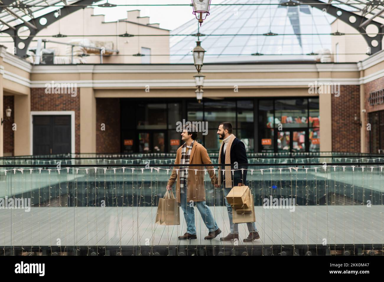 full length of trendy homosexual couple with shopping bags waking near building with stores,stock image Stock Photo