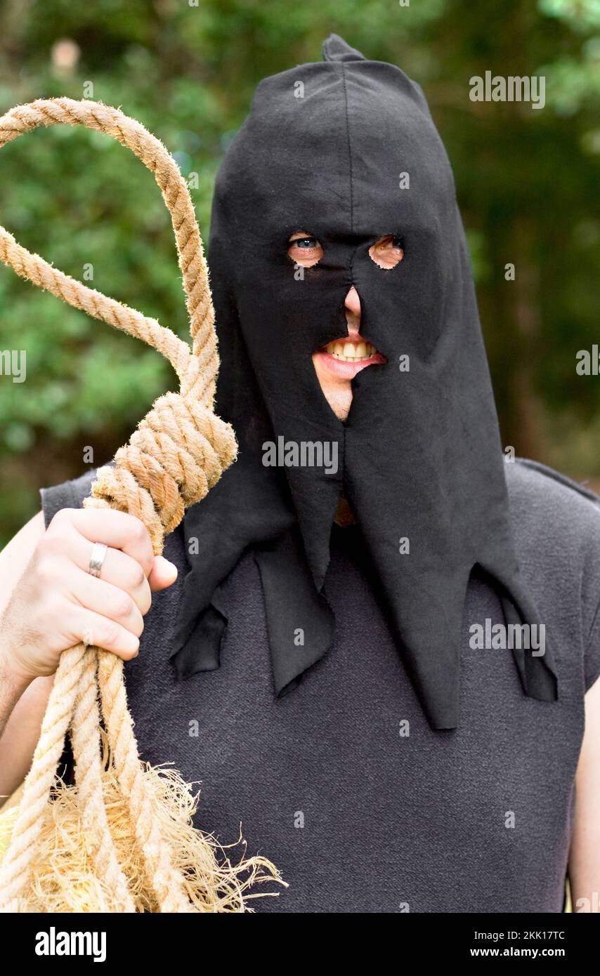 Black Hooded Medieval Hangman Stands With An Look Of Anger And Hatred With Rope Noose At Outdoor Gallows Stock Photo