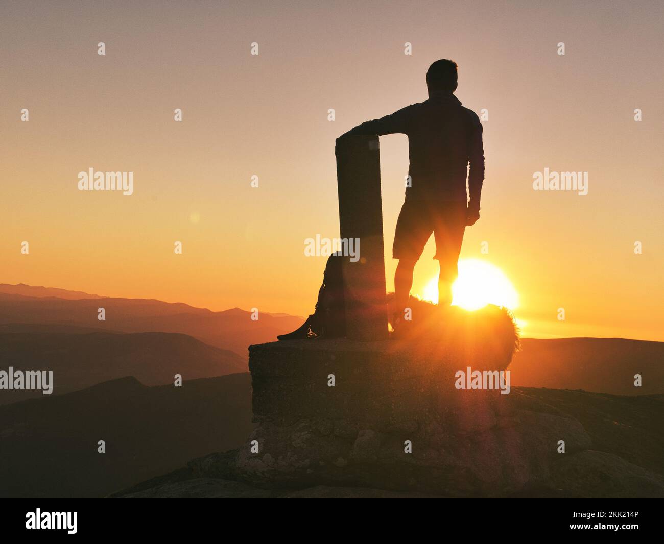The silhouette of a man standing on the peak of a mountain and admiring ...