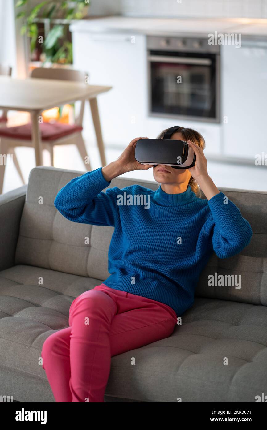 Young woman puts on VR glasses and explores interesting games with amazing graphics at home Stock Photo