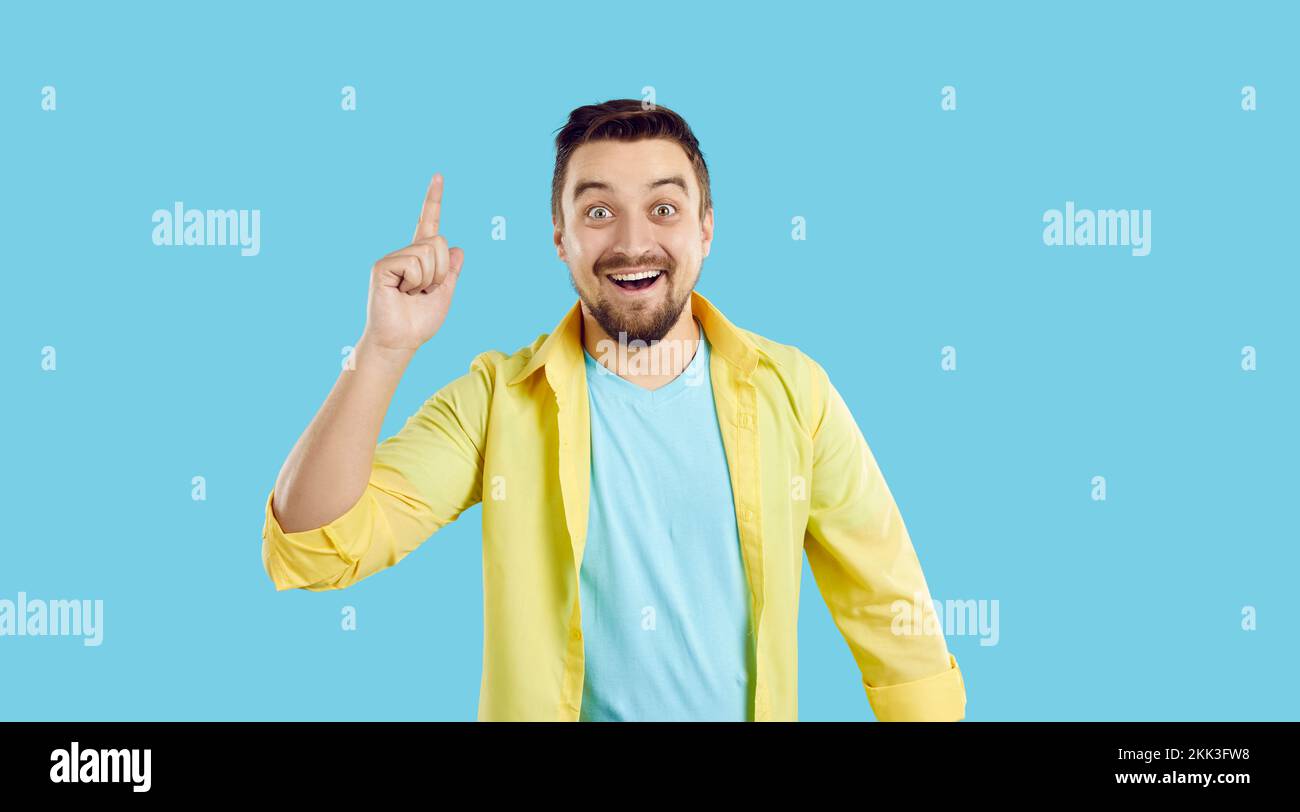Man standing isolated on a blue background has an idea, smiles and points his finger up Stock Photo