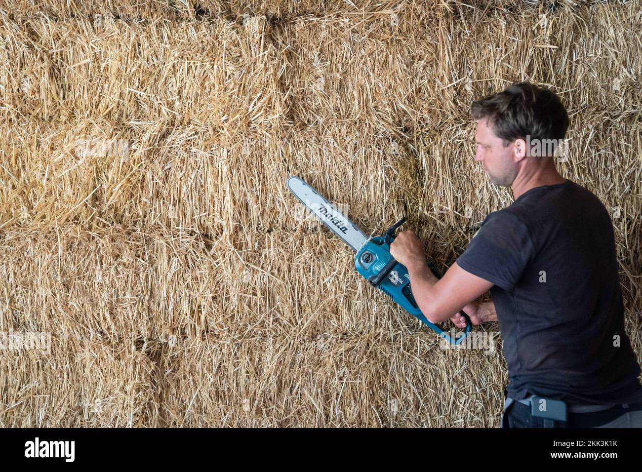 Obernsees, Germany. 26th Aug, 2022. Florian Hoppe, board member at Fachverband Strohballenbau (FASBA e.V.), trims a straw bale wall with an electric chainsaw. Building with clay around straw is an old method, but its sustainability may even make it a model for the future. Credit: Nicolas Armer/dpa/Alamy Live News Stock Photo