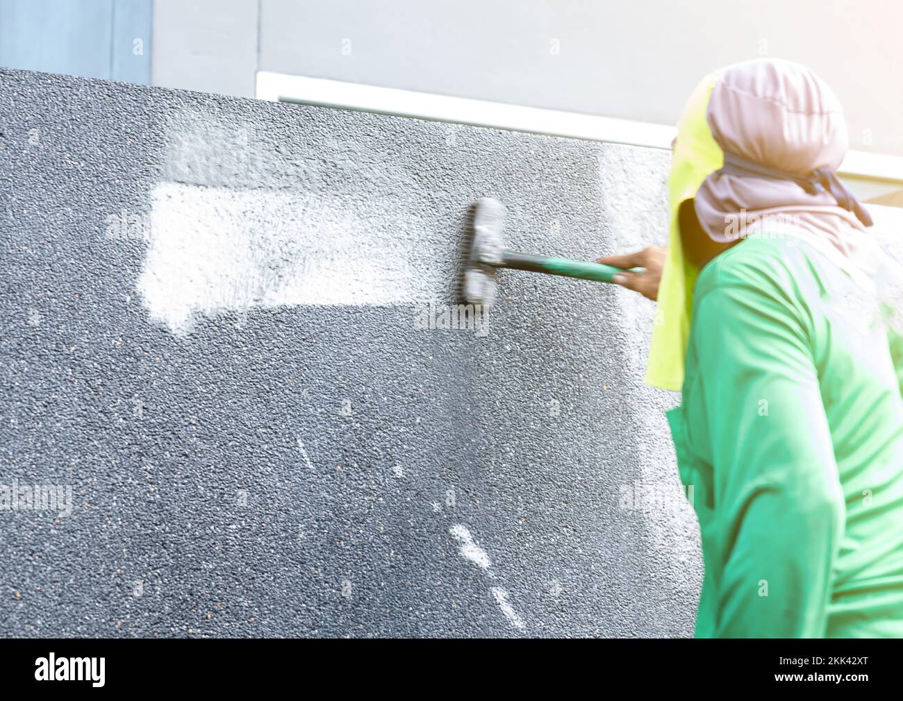 Workers use a brush dipped in hydrochloric acid mixed with water to scrub the surface exposed aggregate finish wall. Stock Photo