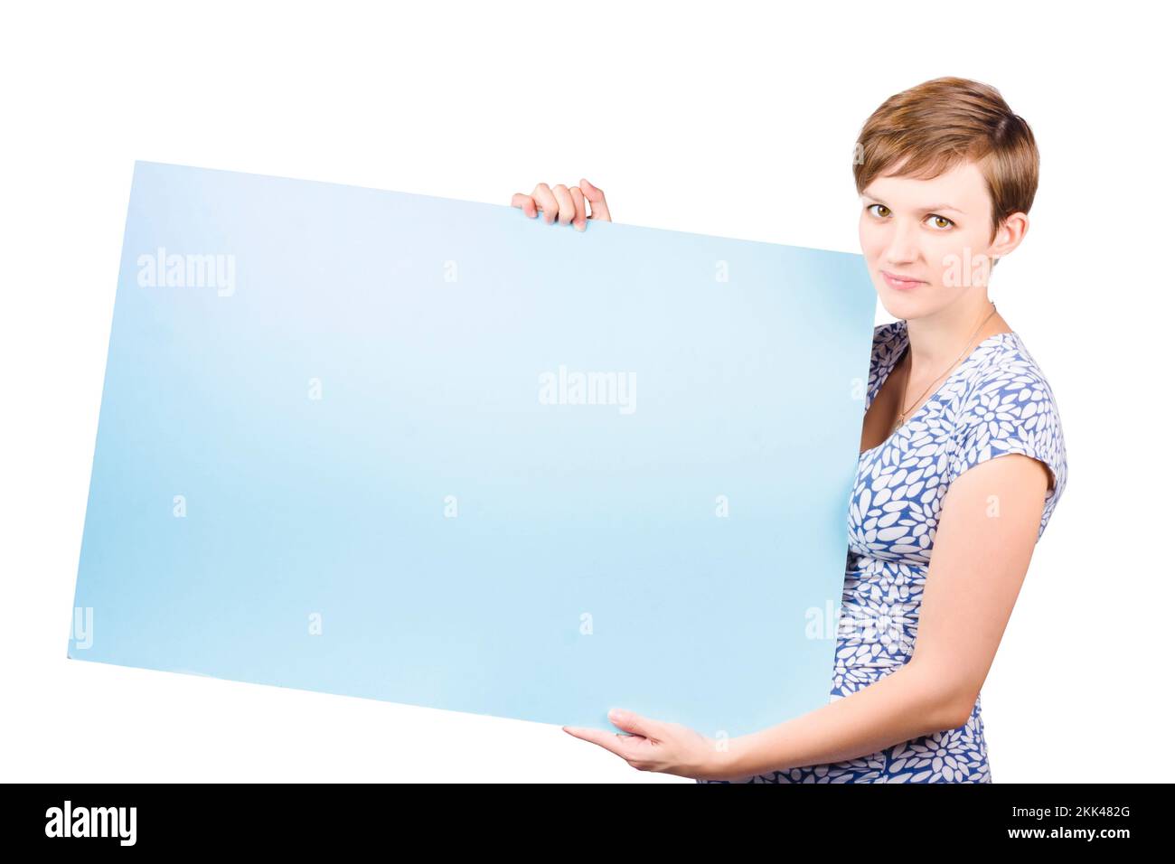 Smiling friendly young woman with short neat hair holding a blank blue rectangular placard to the side with copyspace for your text or advertisement, Stock Photo