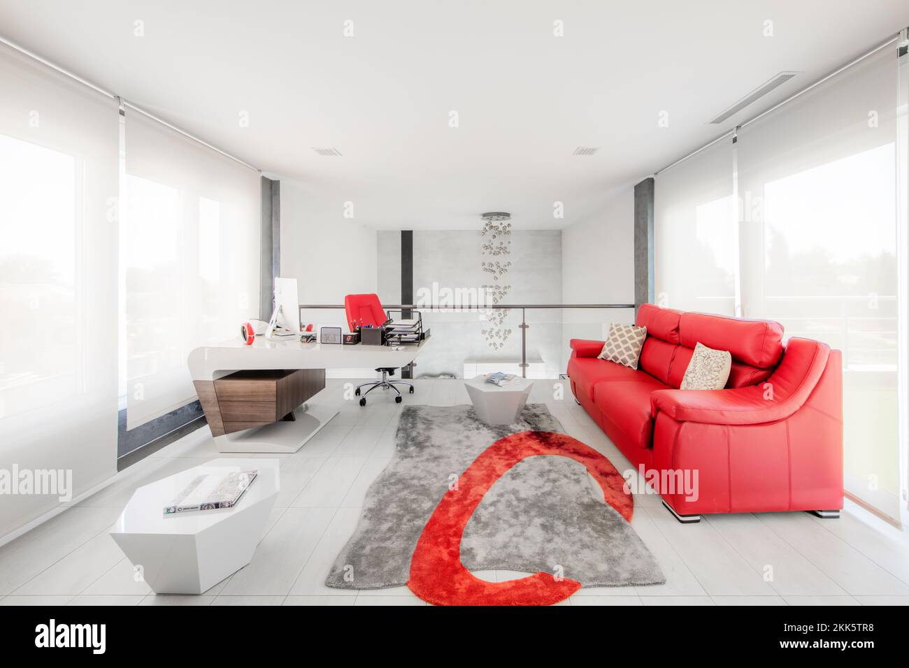 Loft room with desk, bright red leather sofa, designer side tables and