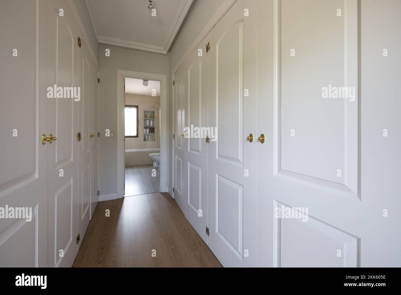 Empty room with white lacquered wooden built-in wardrobes forming a dressing room corridor with access to an en-suite bathroom Stock Photo