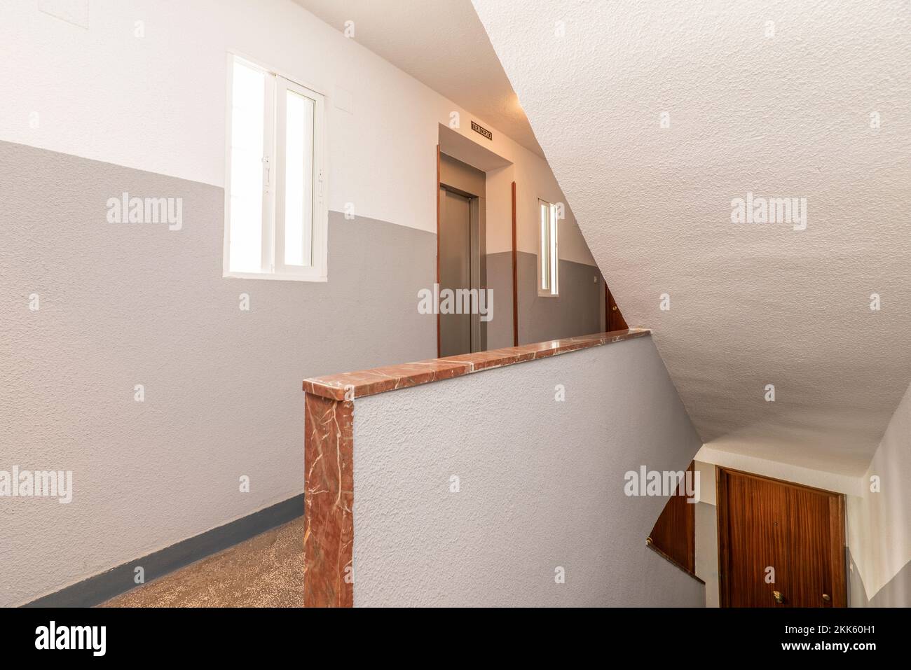 Landing of a residential apartment building with a staircase with reddish terrazzo floors, railings with red marble and a gray metal elevator Stock Photo