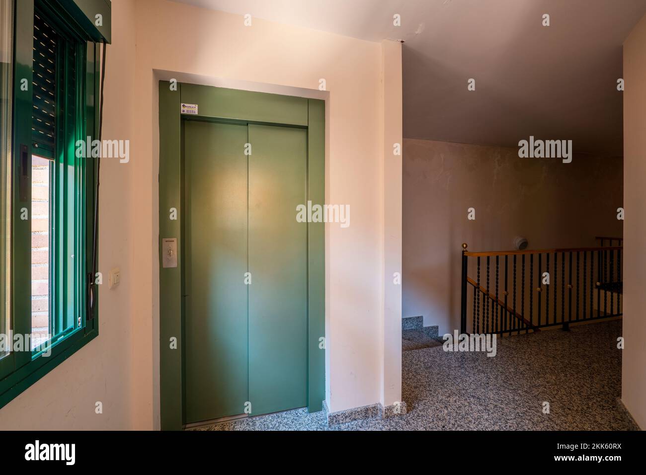 Landing of a residential apartment building with granite floors, black metal railing with wood and a green painted elevator Stock Photo