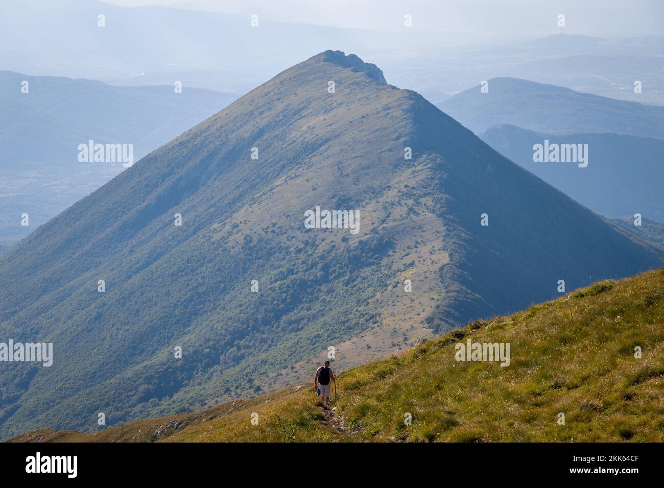 A lone hiker hiking down the mountain path, with a ridge in the background Stock Photo
