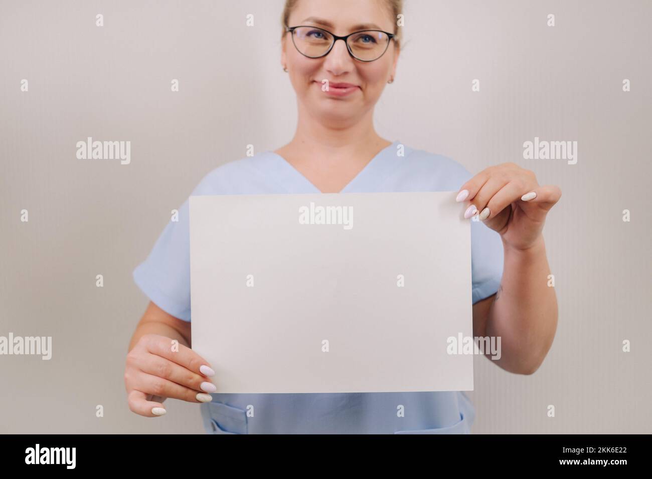 Portrait of a female doctor in a blue robe holding a white blank sheet ...