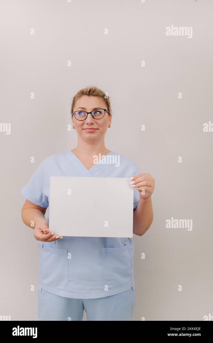 Portrait of a female doctor in a blue robe holding a white blank sheet ...