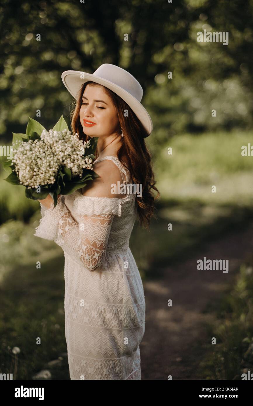 Portrait of a beautiful woman in a white dress and a hat with lilies of ...