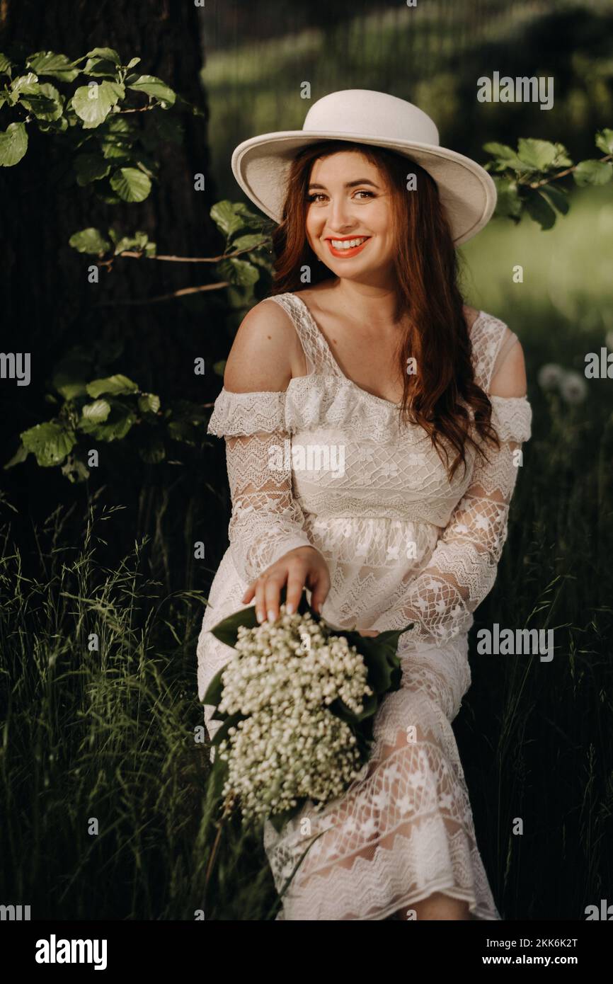 Portrait of a beautiful woman in a white dress and a hat with lilies of ...