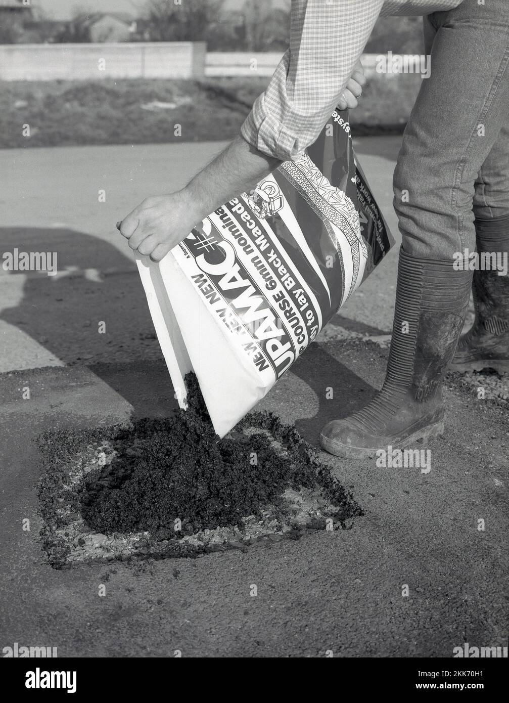 1980s, re-surfacing, a man using a bag of a new construction product to patch or repair a driveway, a ready-mix or ready to lay black tarmacmacadam or asphalt, known as a cold-lay tar, England, UK. Stock Photo