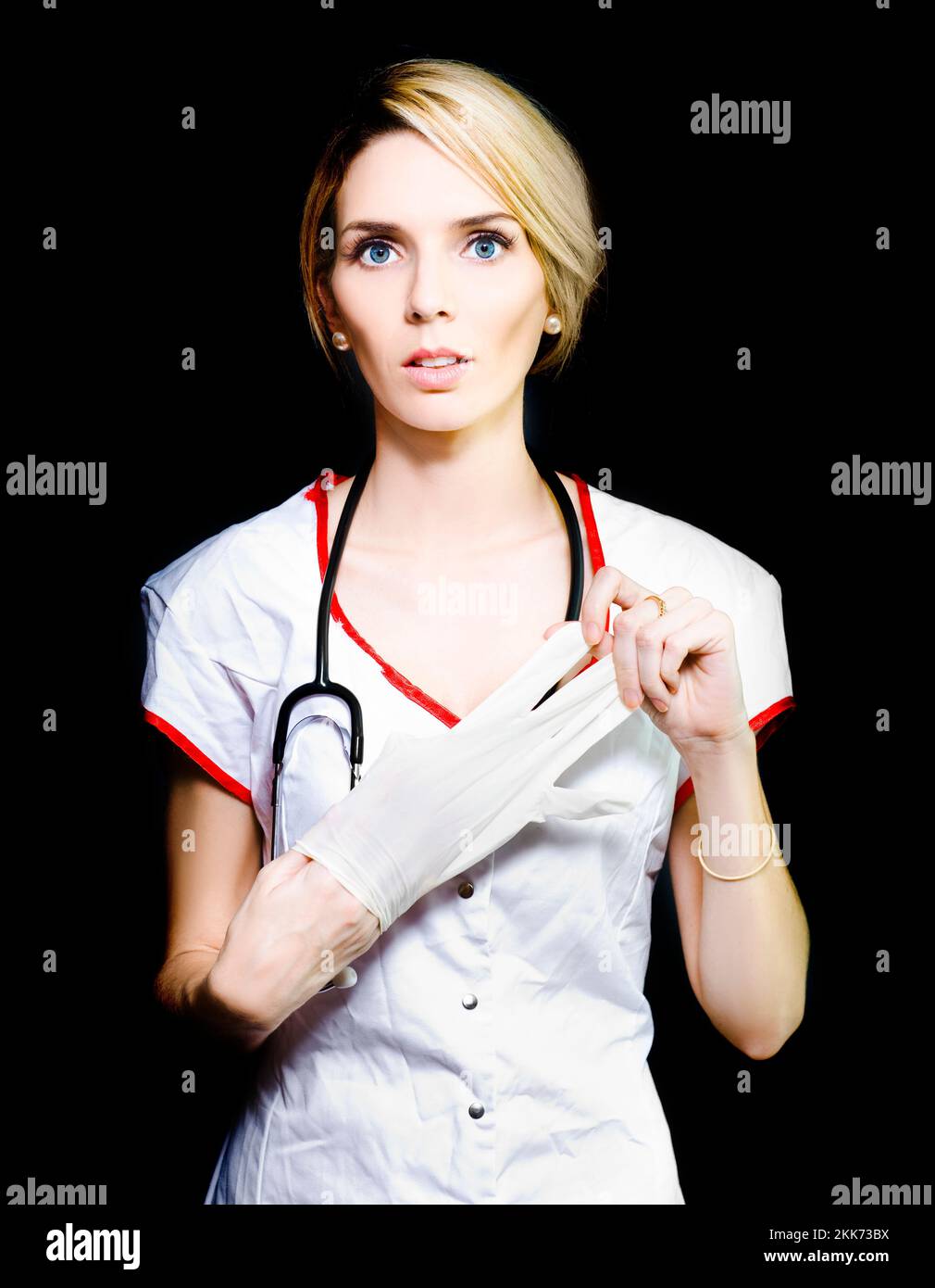 Serious young nurse with short blonde hair removing her latex gloves after doing blood work on a patient Stock Photo