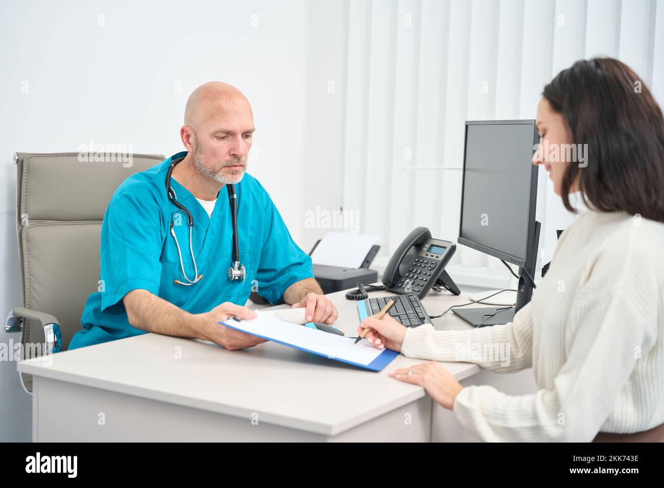 Woman is signing a document at the table of doctor Stock Photo