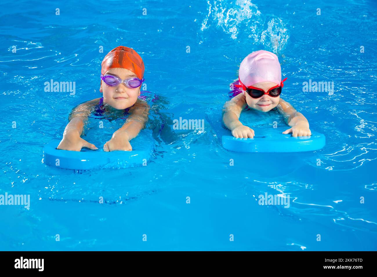 Two little girls learning how to swim in swimming pool using flutter