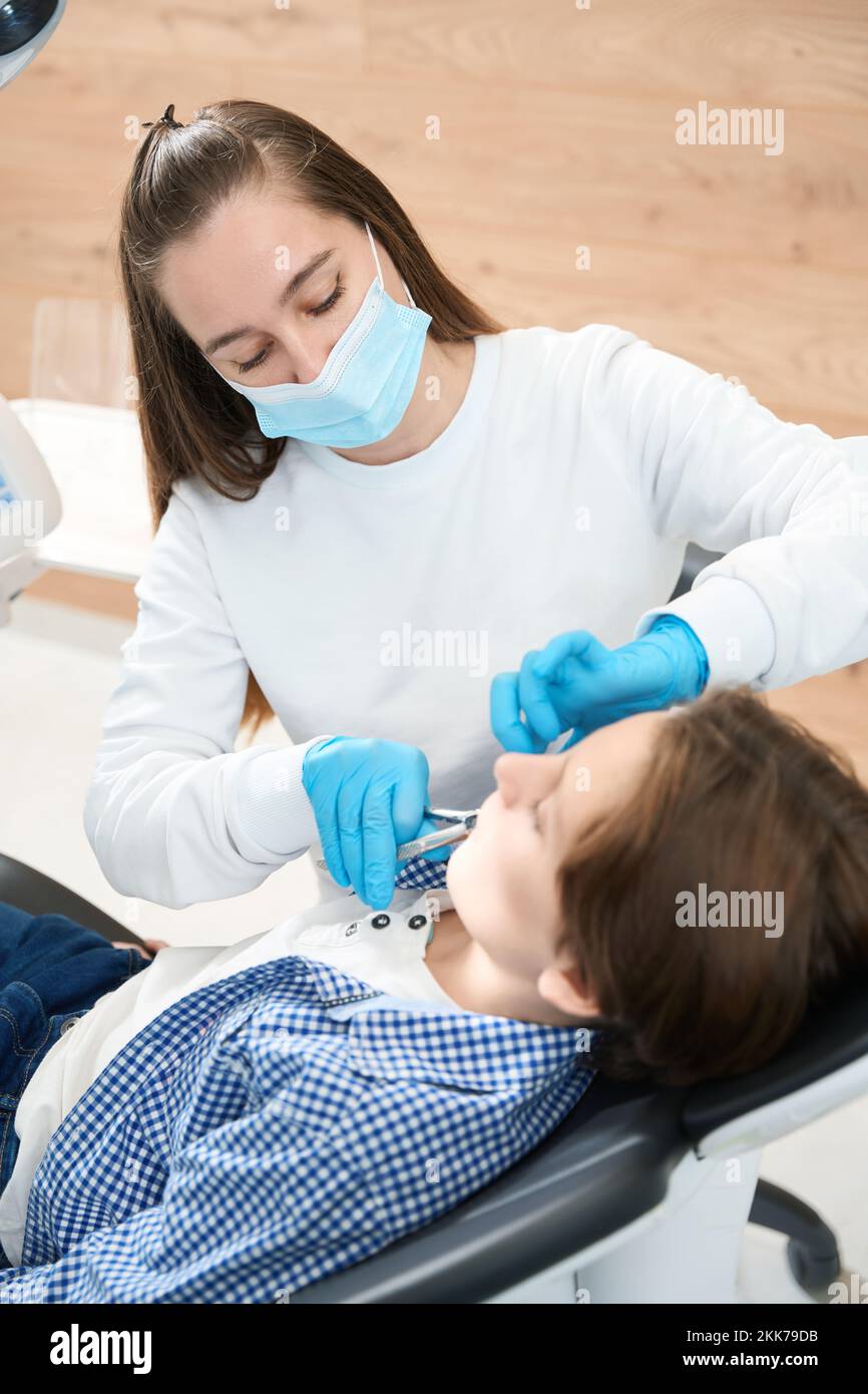 Dentist surgeon removes a tooth to boy with special tool Stock Photo