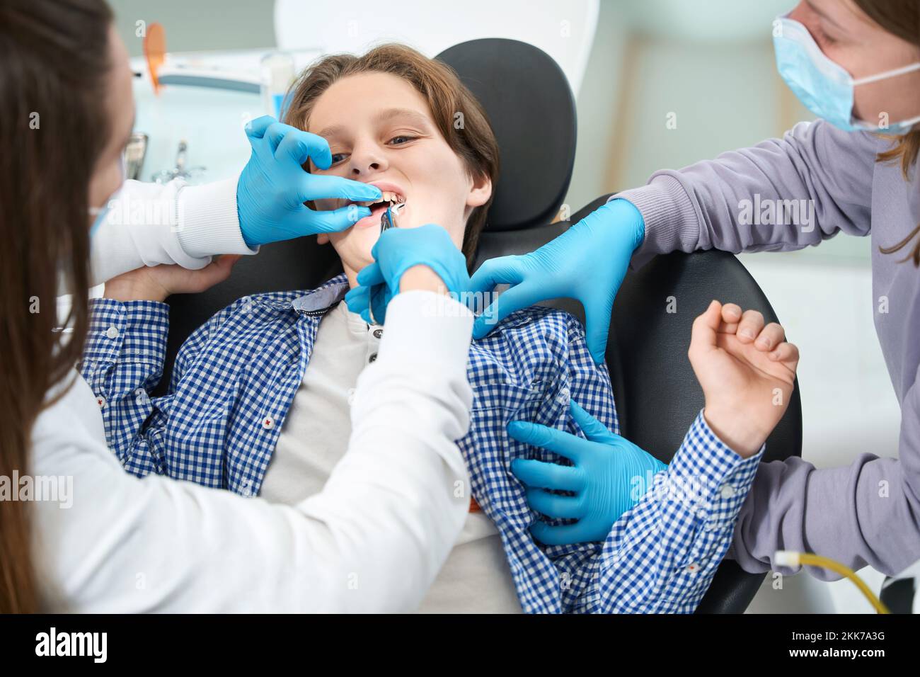 Woman dentist removes tooth to young patient with special tool Stock