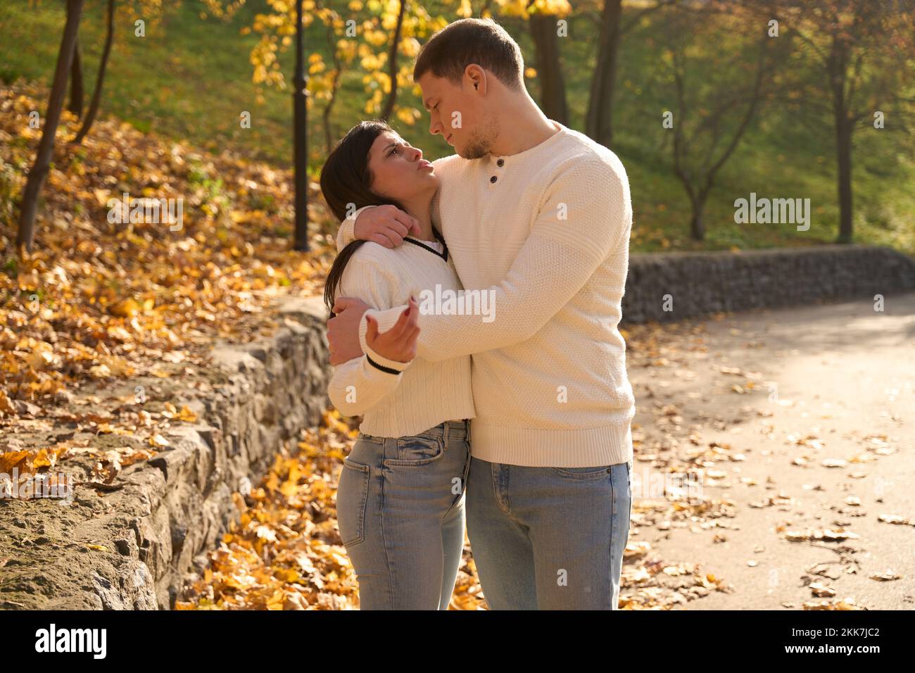 Couple in light sweaters stands, embracing, among the autumn landscape Stock Photo