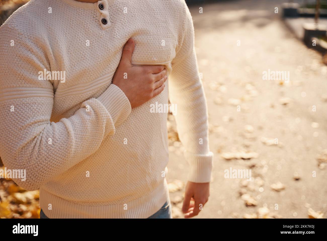 Moung man stands on park alley and holds to his sternum Stock Photo