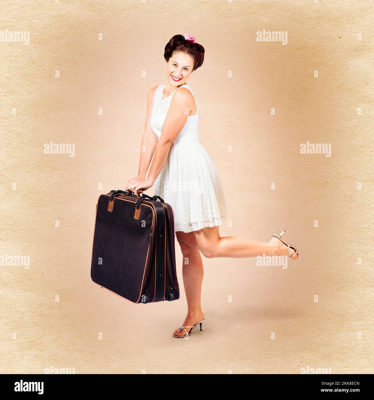 Vintage travel female carrying old fashion suitcase kicking up leg in a square portrait from a retro summer holiday Stock Photo