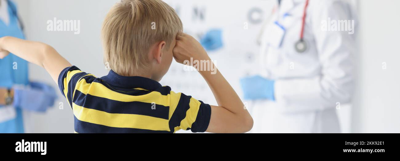 Boy on appointment in clinic, oculist cabinet, sight diagnostic closing eye and say out loud letter on board Stock Photo