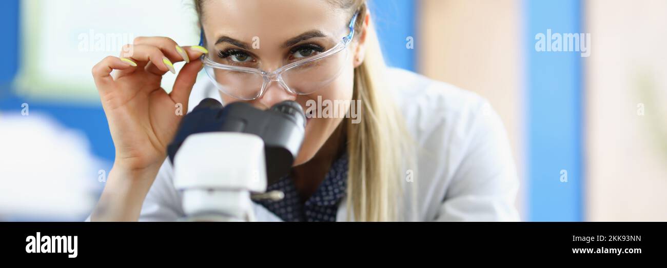 Clever laboratory lady in medical gown investigate sample under microscope tool Stock Photo