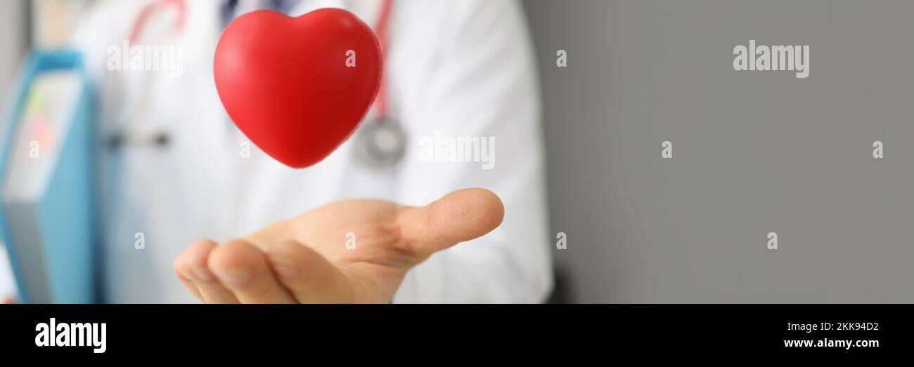 Cardiologist throw red plastic heart and catch it in palm, save life through donation or charity activity Stock Photo