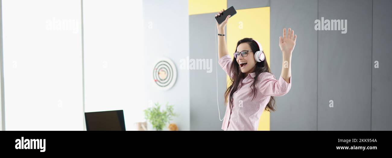 Happy woman dancing on couch, listen to music in headset and sing Stock