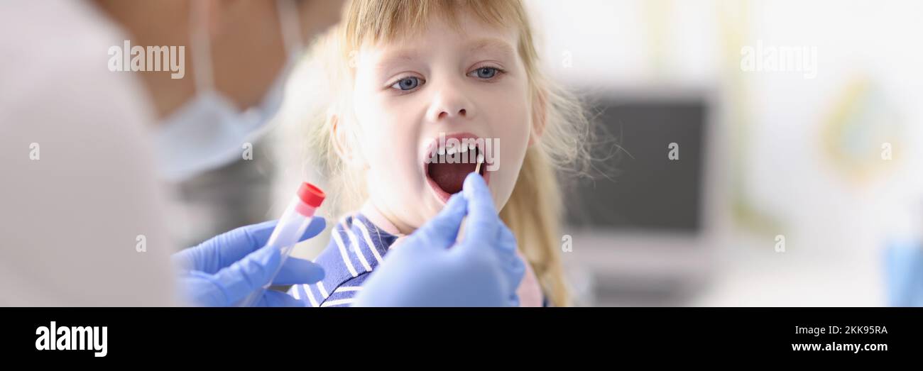 Laboratory assistant in protective suit takes swab from childs throat, procedure at home Stock Photo