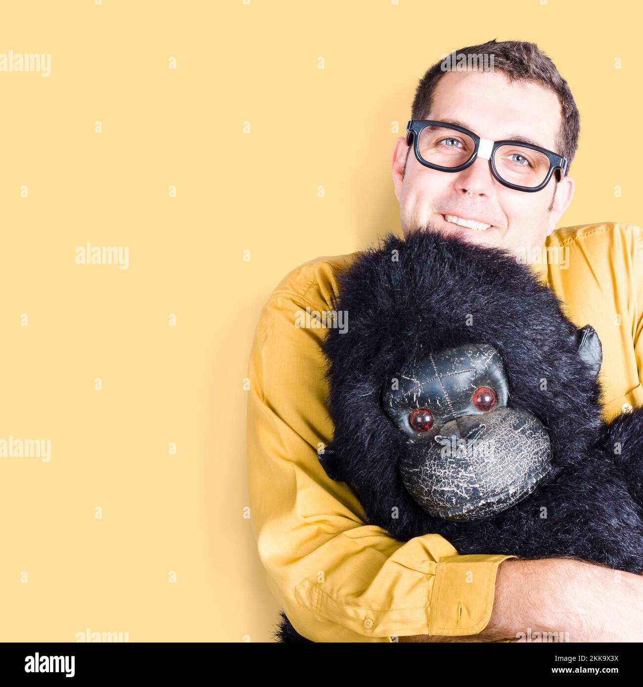 Big goofy man cuddling soft toy gorilla on yellow background. Comfort zone concept Stock Photo