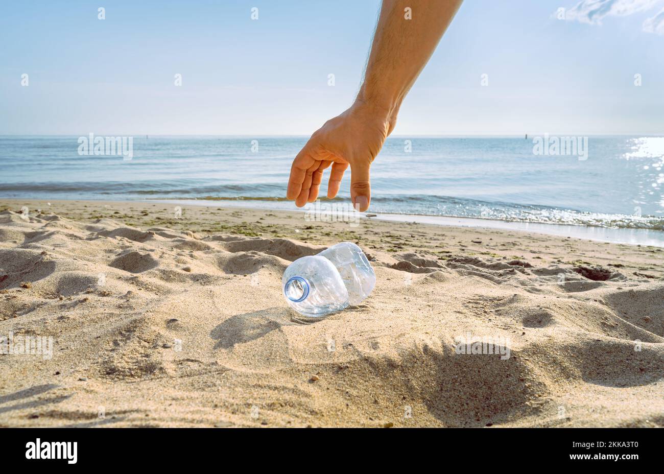 A hand reaches down to pick up a discarded water bottle Stock Photo Alamy