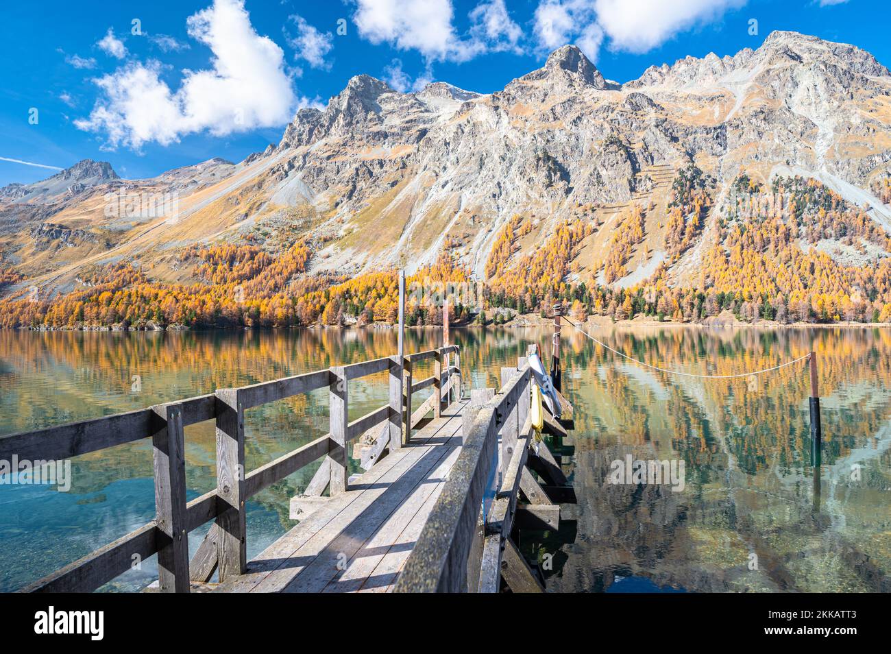 Wooden jetty in the water of Lake Sils, Switzerland with beautiful mountains covered with larix trees in autumn foliage Stock Photo