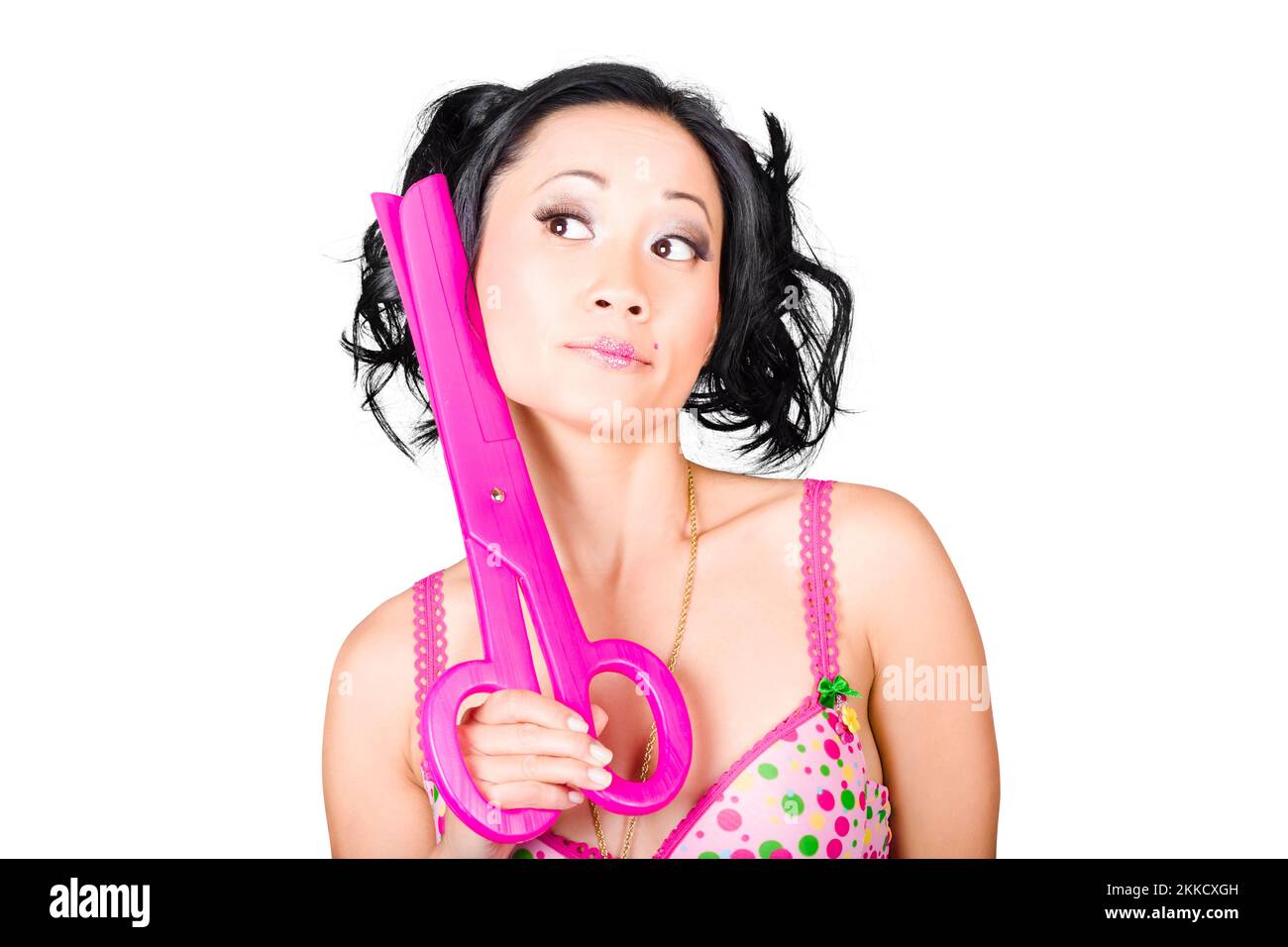 Quirky hairdressing photo of a young woman barber holding large pink scissors while thinking up a retro do Stock Photo