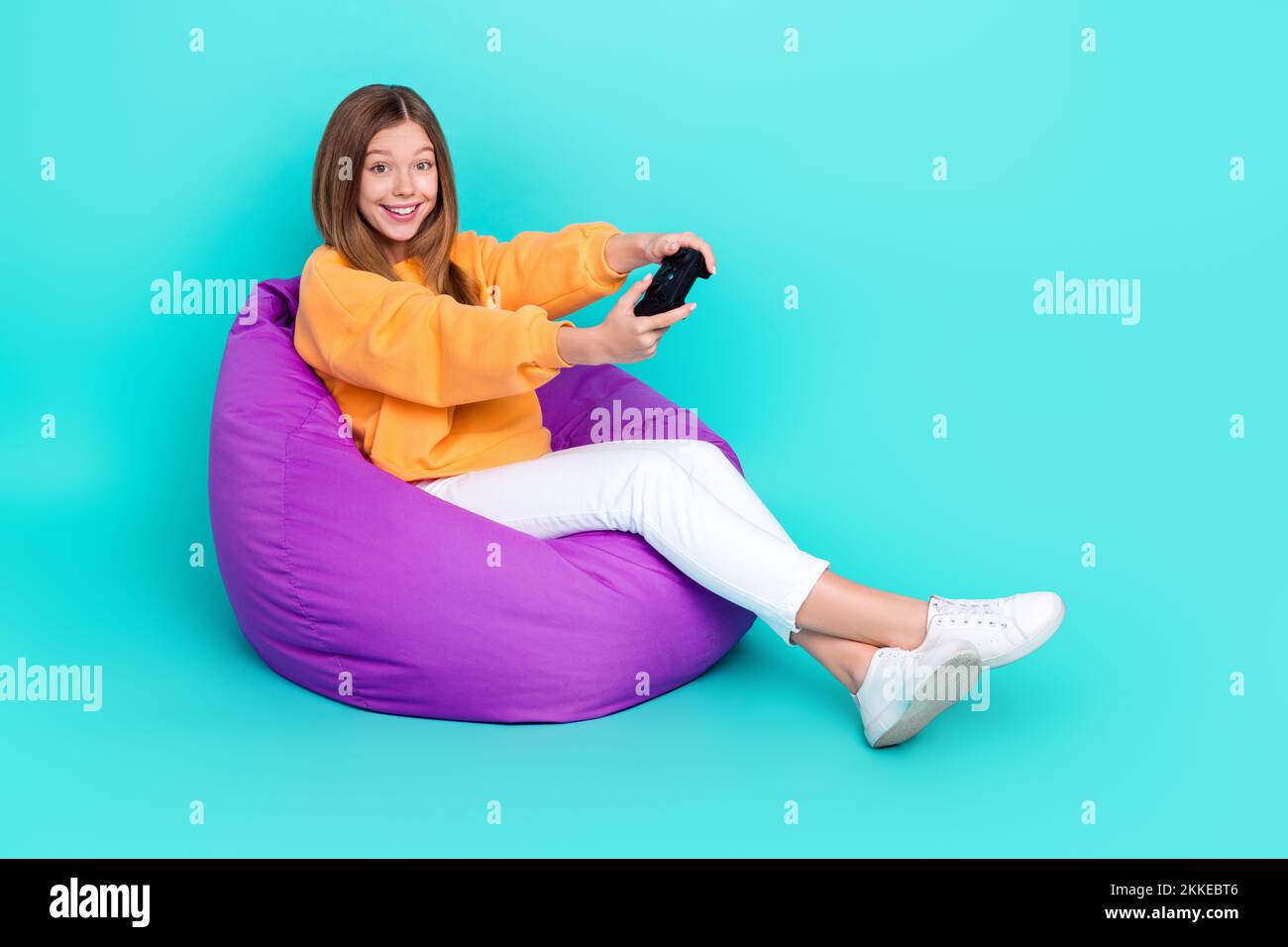 Full length photo of pretty cute school girl dressed orange hoodie bean bag  having fun playstation empty space isolated teal color background Stock  Photo - Alamy