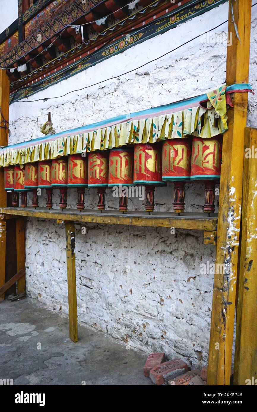 Several identical painted prayer wheels line the wall along a narrow street in Thimphu, Bhutan. The wheels are a common sight around the country. Stock Photo