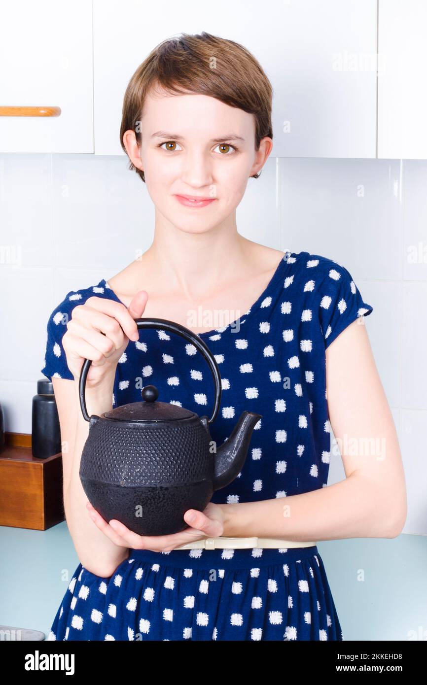 A woman in the kitchen holding a traditional style tea kettle Stock