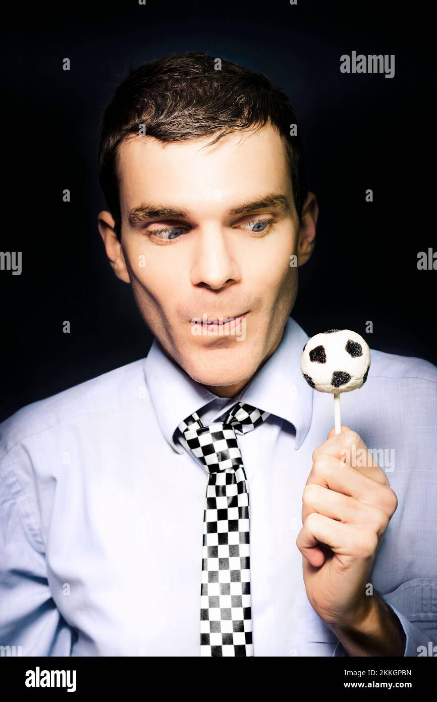Football fanatic business man looking at a candy soccer lollypop with a