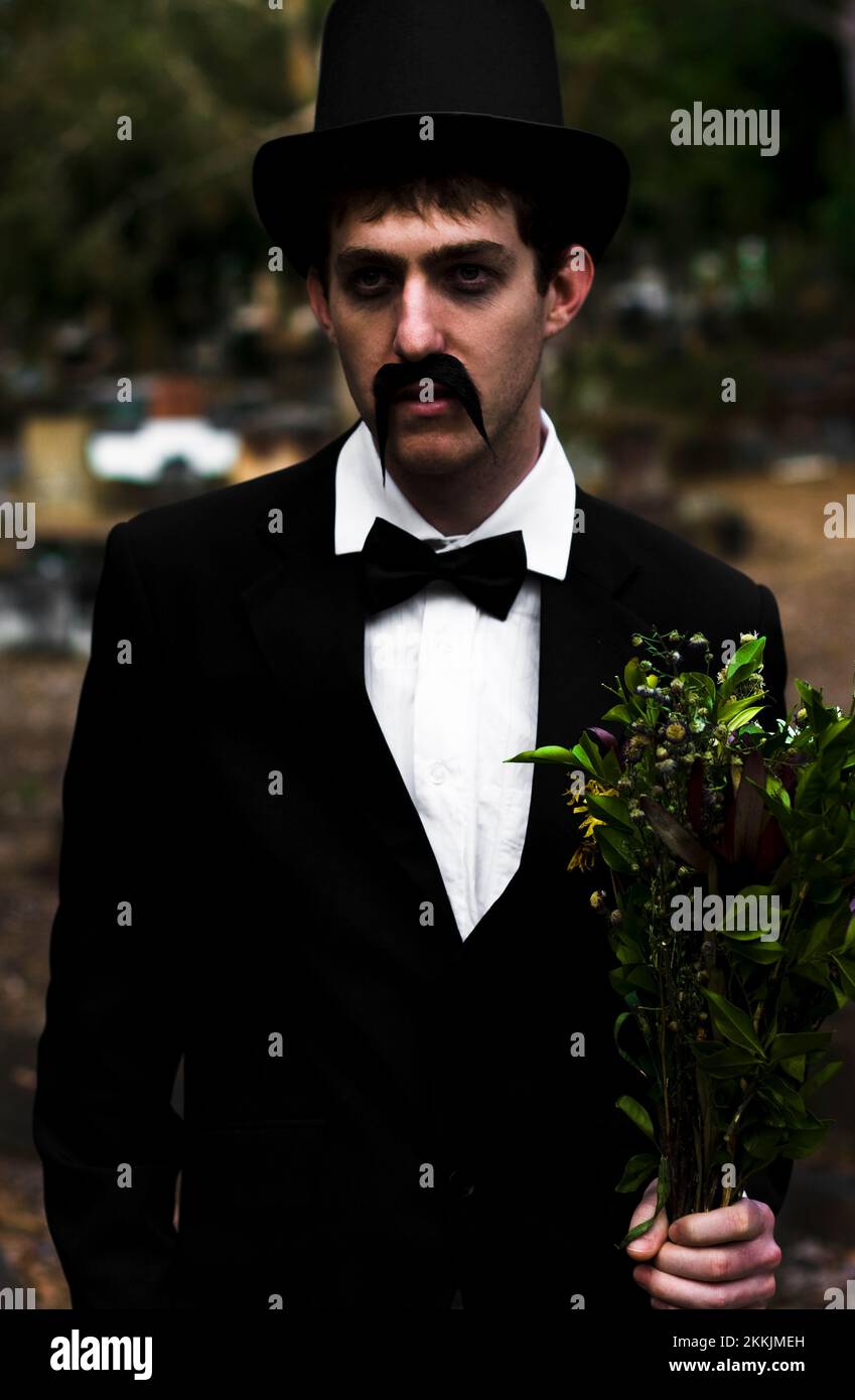 Sad Mourning Man Stands Holding Dead Flowers At A Cemetery Stock Photo