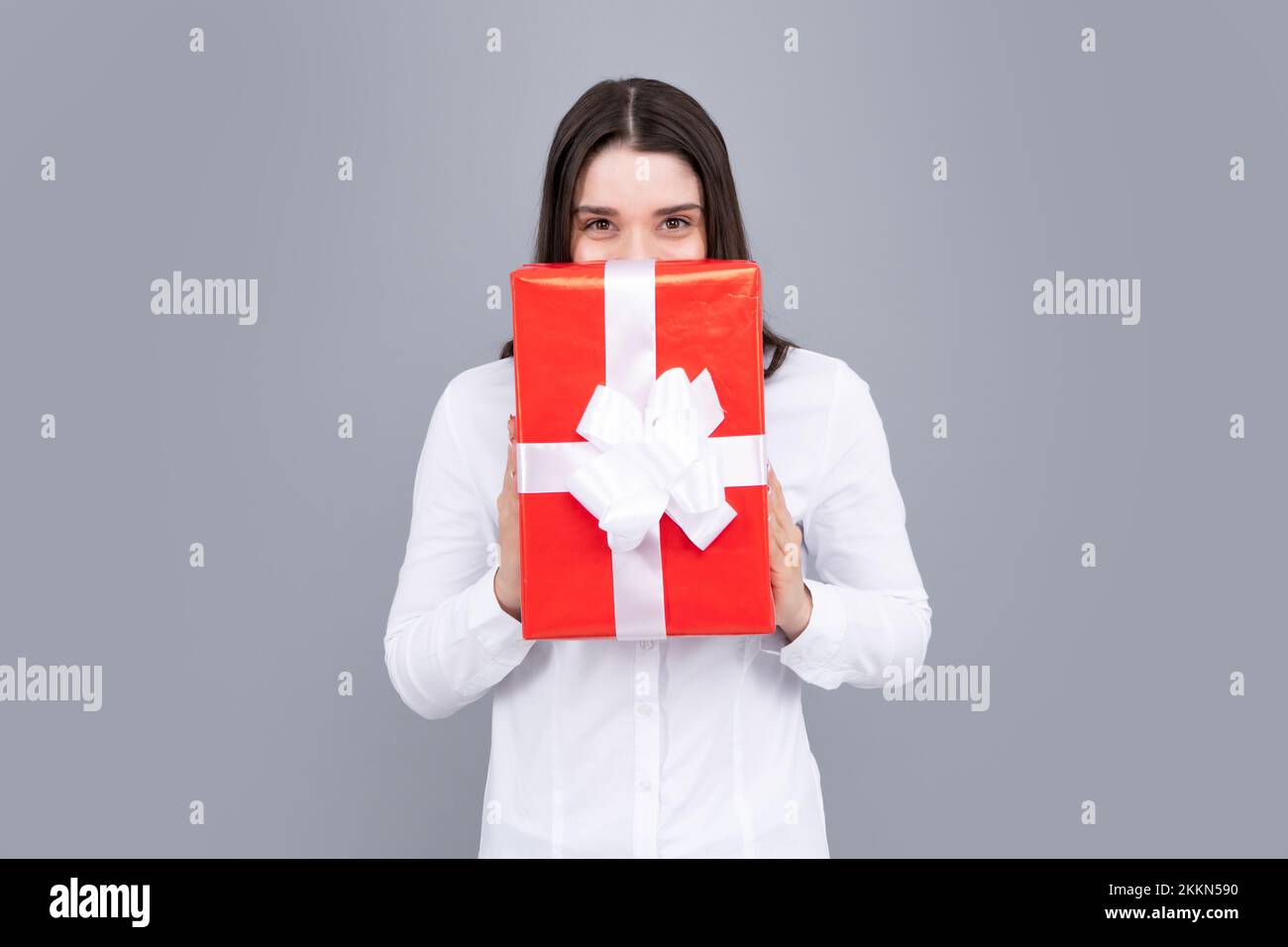 Happy birthday. Woman holding gift box with ribbon. Studio portrait over gray background. Stock Photo