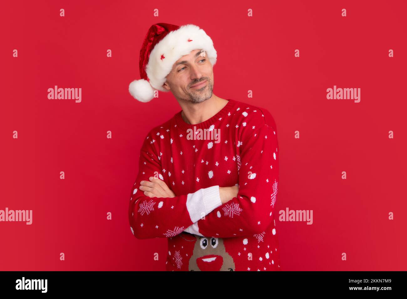 Santa man, studio portrait. Handsome man in a winter sweater and Santa hat on studio red background. Stock Photo